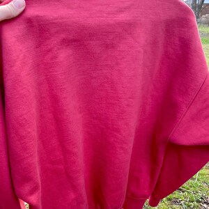 May include: A red sweatshirt with a navy blue ribbed collar. The sweatshirt is made of a soft, comfortable material.