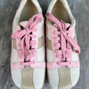 K&ouml;nnte beinhalten: Ein Paar cremefarbene Sneaker mit rosa Wildlederakzenten und rosa Schn&uuml;rsenkeln. Die Sneaker haben eine wei&szlig;e Gummisohle.