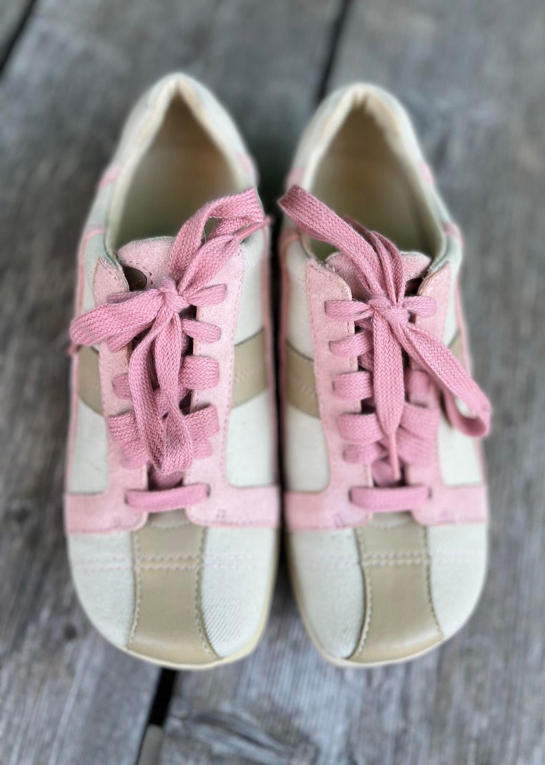 K&ouml;nnte beinhalten: Ein Paar cremefarbene Sneaker mit rosa Wildlederakzenten und rosa Schn&uuml;rsenkeln. Die Sneaker haben eine wei&szlig;e Gummisohle.