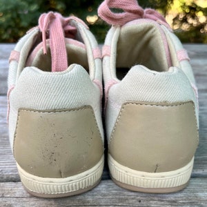 K&ouml;nnte beinhalten: Ein Paar cremefarbene Canvas-Sneaker mit rosafarbenen Schn&uuml;rsenkeln. Die R&uuml;ckseite der Schuhe hat eine hellbraune Lederplatte.