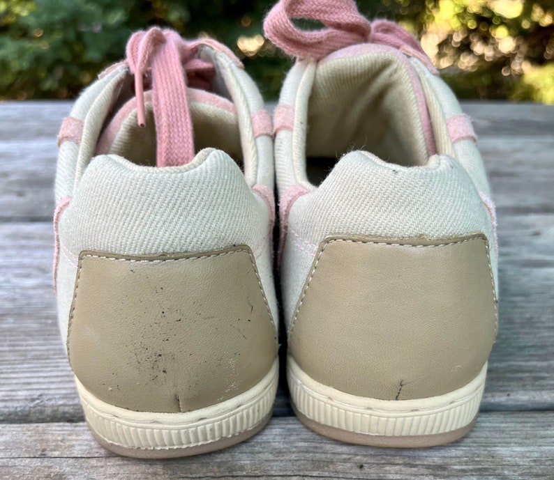 K&ouml;nnte beinhalten: Ein Paar cremefarbene Canvas-Sneaker mit rosafarbenen Schn&uuml;rsenkeln. Die R&uuml;ckseite der Schuhe hat eine hellbraune Lederplatte.