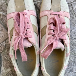 K&ouml;nnte beinhalten: Ein Paar hellbeige Sneaker mit rosa Schn&uuml;rsenkeln. Die Sneaker haben ein rosa Wildleder-Panel an der Spitze und ein beige Canvas-Panel an der Seite.