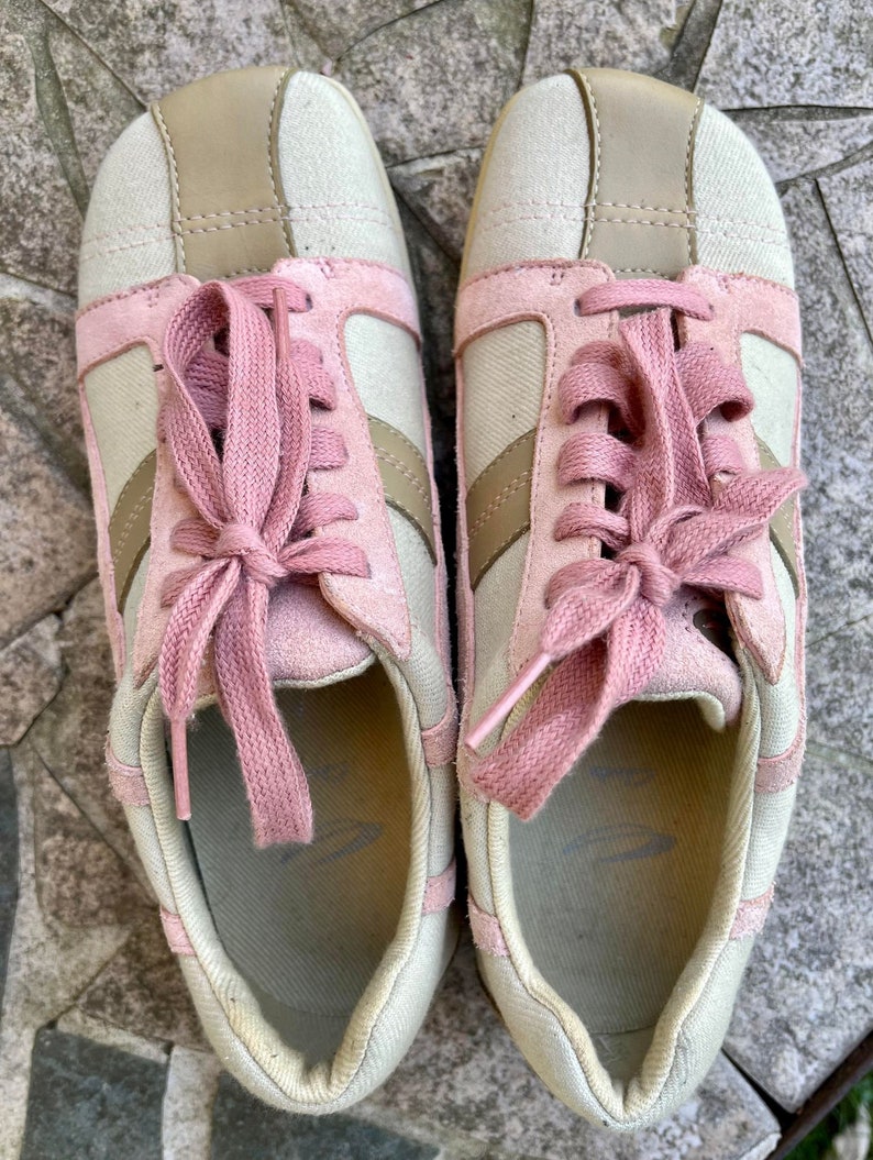 K&ouml;nnte beinhalten: Ein Paar hellbeige Sneaker mit rosa Schn&uuml;rsenkeln. Die Sneaker haben ein rosa Wildleder-Panel an der Spitze und ein beige Canvas-Panel an der Seite.