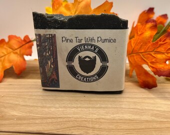 Peut inclure: Un savon brun foncé avec une étiquette blanche qui indique "Pine Tar With Pumice" et un logo qui dit "Vienna's Creations" avec un visage d'homme barbu au centre.