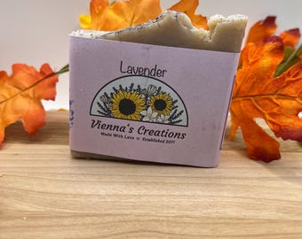 May include: A bar of lavender soap with a purple and white label that says "Lavender" and "Vienna's Creations" with a sunflower design. The soap is on a wooden surface with fall leaves.