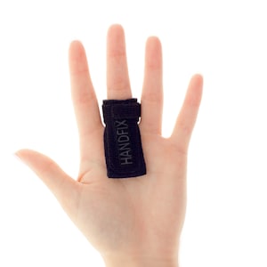 以下が含まれることがあります： 「HANDFIX」と印刷された黒い指の固定具。固定具は人の手の真ん中の指に装着されています。