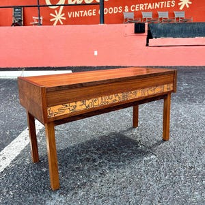 May include: A mid-century modern rosewood side table with a geometric inlay design. The table has a rectangular top and four legs.