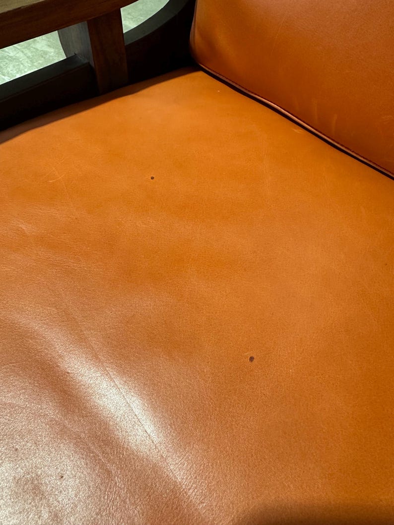 May include: Close-up of a brown leather chair seat with two small dark spots.
