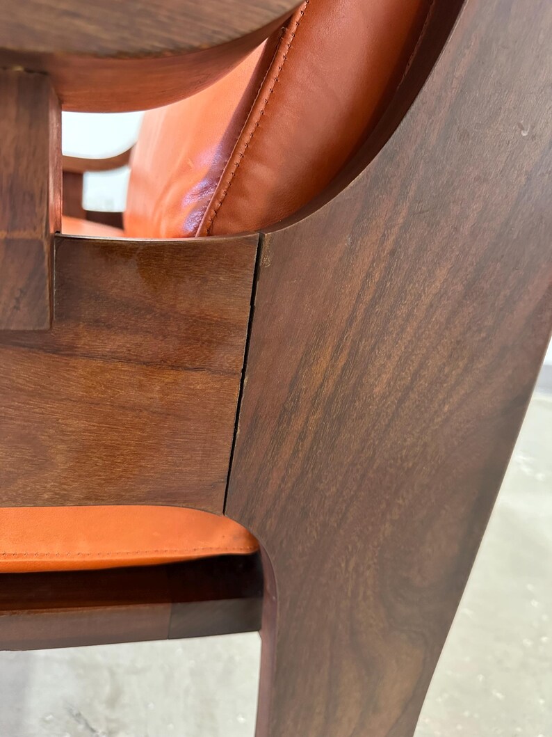 May include: Close-up of a wooden chair with a curved back and orange leather upholstery. The chair is made of dark wood with a smooth finish.
