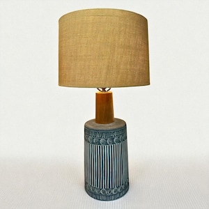 May include: A vintage table lamp with a tan fabric shade. The lamp base is cylindrical, with a dark teal and white striped pattern. The lamp has a wooden neck and a tan lampshade.