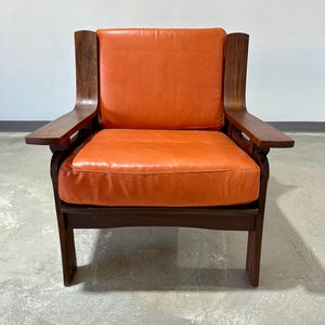 May include: A mid-century modern armchair with a dark wood frame and orange leather upholstery.