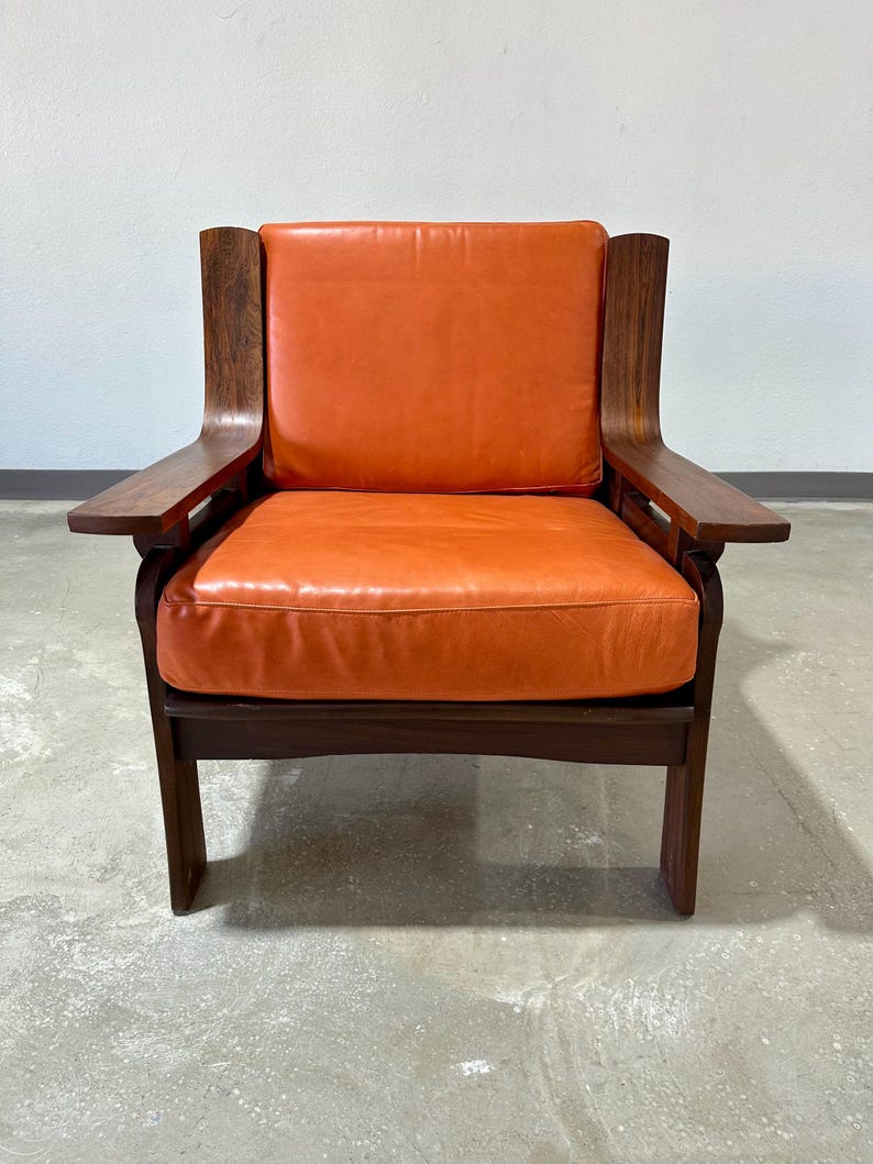 May include: A mid-century modern armchair with a dark wood frame and orange leather upholstery.