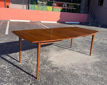May include: A mid-century modern dining table with a rich, warm wood finish. The rectangular table has a smooth surface and tapered legs. The table is approximately 183 cm long and 91 cm wide.