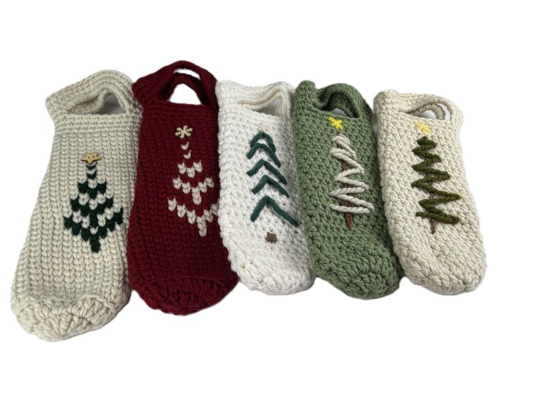 Pu&ograve; includere: Cinque copribottiglie all'uncinetto con manici, ognuno caratterizzato da un diverso disegno di albero di Natale ricamato. Le coperture sono color crema, rosso scuro, bianco, verde salvia e crema, con alberi in filati contrastanti e stelle gialle.