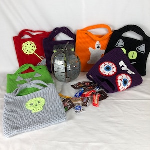 May include: Six crocheted Halloween trick-or-treat bags with different designs, including a ghost, a skull, a cat, and an eye. The bags are filled with candy.