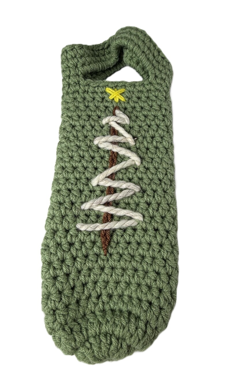 Pu&ograve; includere: Una borsa per bottiglia all'uncinetto color verde salvia con un manico sulla parte superiore. La parte anteriore &egrave; decorata con una linea verticale marrone ricamata che rappresenta un tronco d'albero, con zigzag in filo bianco e una stella.