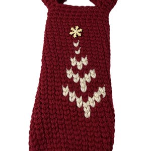 Pu&ograve; includere: Una borsa per bottiglia di vino all'uncinetto di colore rosso scuro con un manico sulla parte superiore e un motivo a forma di albero di Natale cucito color crema sul davanti. Una piccola decorazione in legno a forma di fiocco di neve &egrave; applicata.