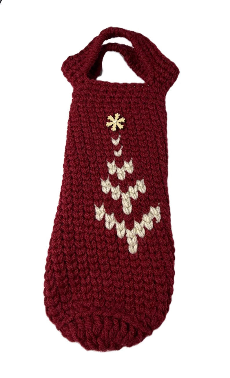 Pu&ograve; includere: Una borsa per bottiglia di vino all'uncinetto di colore rosso scuro con un manico sulla parte superiore e un motivo a forma di albero di Natale cucito color crema sul davanti. Una piccola decorazione in legno a forma di fiocco di neve &egrave; applicata.
