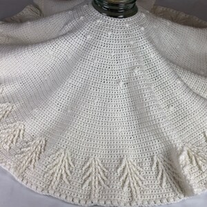 May include: White crocheted tree skirt with a scalloped edge and a beaded center. The skirt has a fringe around the bottom edge.