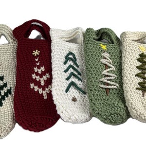 Pu&ograve; includere: Cinque borse per bottiglie realizzate a mano all'uncinetto con manici, caratterizzate da vari disegni di alberi di Natale. Le borse sono nei colori crema, bordeaux, bianco e verde salvia, con motivi ad albero ricamati e stelle in legno.