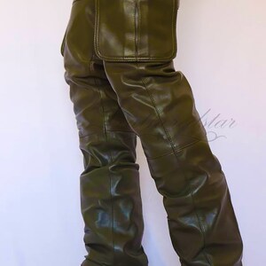 May include: Olive green leather cargo pants with a large cargo pocket on the right leg. The pants are worn with brown cowboy boots.