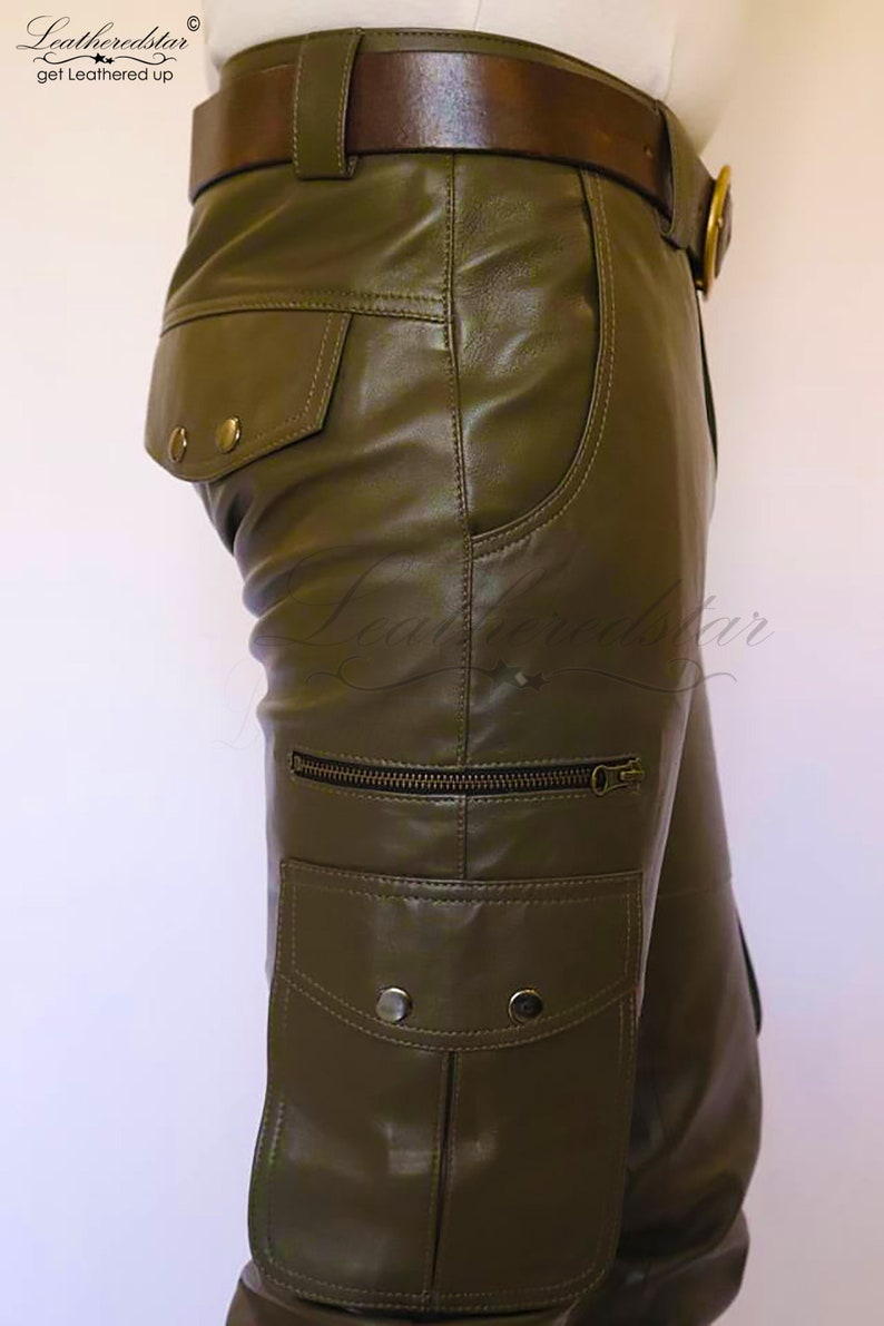 May include: Olive green leather cargo pants with a brown leather belt and a zippered pocket on the side. The pants have a flap pocket with two button closures on the back.