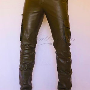 May include: Olive green leather cargo pants with a brown leather belt and brown leather boots. The pants have a zippered pocket on the side and a flap pocket on the thigh.