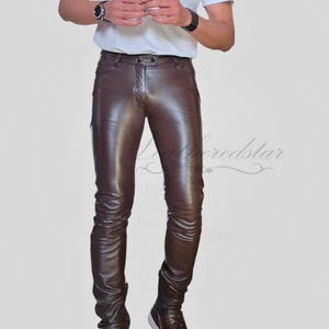 May include: A person wearing brown leather trousers with a white t-shirt and brown shoes. The trousers are slim fitting and have a shiny finish. The text "Leatherstar get leathered up" is visible in the top right corner of the image.