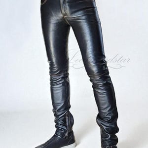 May include: Black leather trousers with visible stitching and a zip detail at the ankle. The trousers are worn with black trainers with white soles. The image has the text "Leatherdstar" and "get Leathered up".