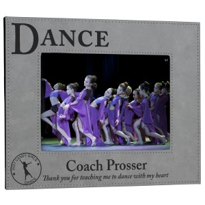 May include: A gray leatherette picture frame with a photo of a group of young girls in purple dresses dancing. The frame has the word "DANCE" at the top and the text "Coach Prosser Thank you for teaching me to dance with my heart" at the bottom. A circular sticker with a star, the words "2021 CANDY GIRLS", and a silhouette of a dancer is in the bottom left corner.