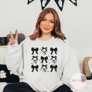 May include: A white sweatshirt with a black and white skull and bow print. The print features multiple skulls with bows on their heads. The skulls are surrounded by black bats.