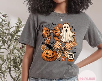 May include: Grey t-shirt featuring a Halloween design with orange bows, a ghost, a carved pumpkin, and the words "Trick or Treat" in a crystal ball. The shirt has short sleeves and a loose fit.