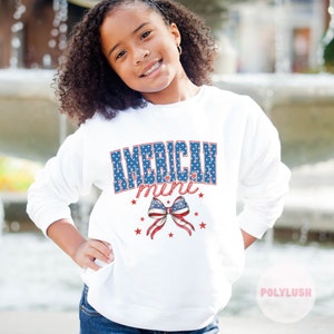 Könnte beinhalten: Weißer Pullover mit einer blauen und roten Grafik, auf der "AMERICAN mini" mit einer rot-weiß-blauen Schleife und Sternen steht.