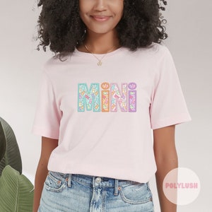 Könnte beinhalten: Rosa T-Shirt mit dem Wort "MINI" in bunten Buchstaben. Jeder Buchstabe ist mit einem Muster aus kleinen, bunten Comic-Tieren gefüllt.