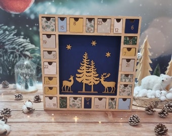 May include: A wooden advent calendar with 24 numbered drawers. The central panel is blue, with gold deer, trees, and stars. The drawers are decorated with various patterns and colours, ideal for the festive season.