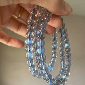 May include: Three light blue beaded bracelets. Each bracelet is made of round, translucent beads with iridescent blue and purple flashes. The bracelets are strung on a thin, clear cord and are held up against a neutral background.