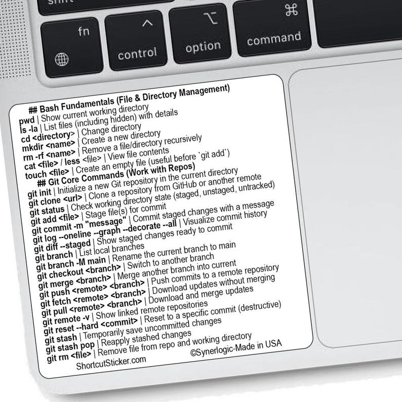 May include: A white sticker with black text, placed on a laptop keyboard. The sticker lists Bash and Git commands, including directory management and Git core commands. The text includes "ShortcutSticker.com" and "Synerlogic-Made in USA".