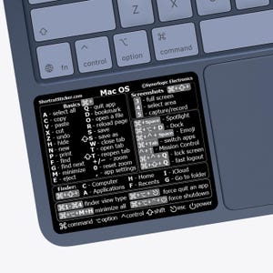May include: A black rectangular sticker with white text applied to a blue keyboard. The sticker lists Mac OS keyboard shortcuts, including sections for Basics, Screenshots, and Finder commands, with symbols for command, option, control, and shift.