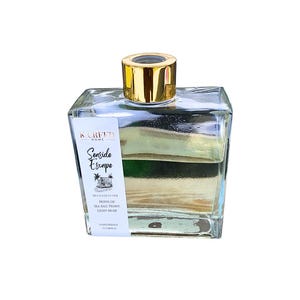 May include: A clear glass bottle with a gold lid filled with a light yellow liquid. The bottle has a white label with the text "KOREED HOME Senside Escape REED DIFFUSER NOTES OF SEA SALT, PEONY, LIGHT MUSK HANDMADE FLORIDA".