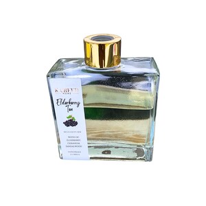 May include: A clear glass bottle with a gold lid filled with a light yellow liquid. The bottle has a white label that reads "K. Creed Home Elderberry Tea Reed Diffuser Notes of Elderberry, Geranium, Sandalwood Handmade Florida"