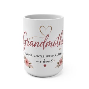 Könnte beinhalten: Weiße Keramiktasse mit dem Wort "Grandmother" in Schreibschrift, einem Herz-Grafik und floralen Akzenten. Die Tasse hat auch die Worte "Loving. Gentle. Irreplaceable. our heart."