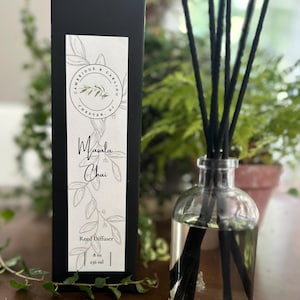 May include: A black box with a white label that reads "Cambridge & Carling, Chester, NJ" and "Masala Chai Reed Diffuser, 8 oz, 236 ml". A clear glass bottle with black reeds is filled with a clear liquid. The bottle is sitting on a wooden surface.