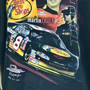 Op de afbeelding: Zwart T-shirt met een NASCAR-raceauto met nummer 8 en de woorden "Bass Pro Shops" en "Martin Truex Jr." Het shirt heeft ook de woorden "Monte Carlo" en diverse sponsorlogo's.