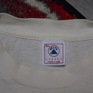 May include: White cotton t-shirt tag with a white triangle logo that says "Delta" and "Cotton made in USA". The tag also says "XL".