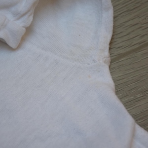 Op de afbeelding: Close-up van een wit shirt met lange mouwen. De stof lijkt een zacht, lichtgewicht materiaal te zijn. De manchet van de mouw is zichtbaar, samen met de schoudernaad. Het shirt is effen en heeft een eenvoudig ontwerp.