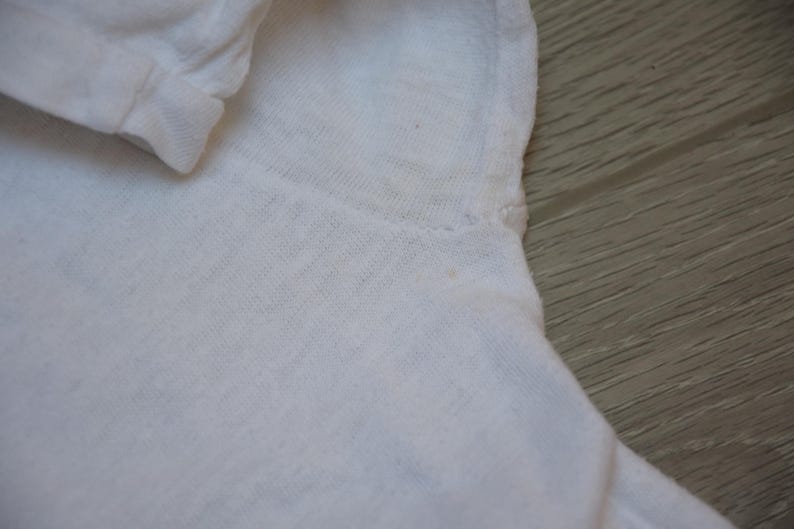 Op de afbeelding: Close-up van een wit shirt met lange mouwen. De stof lijkt een zacht, lichtgewicht materiaal te zijn. De manchet van de mouw is zichtbaar, samen met de schoudernaad. Het shirt is effen en heeft een eenvoudig ontwerp.