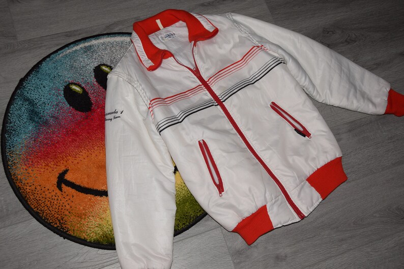 May include: White jacket with red and black stripes. The jacket has a zipper closure and two pockets. The text "remarkable" is printed on the left sleeve.