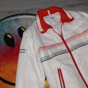 May include: White and red striped jacket with a zipper closure. The jacket has black stripes and the text "Formula 1 Racing Team" on the left sleeve.