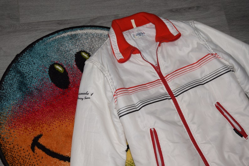 May include: White and red striped jacket with a zipper closure. The jacket has black stripes and the text "Formula 1 Racing Team" on the left sleeve.