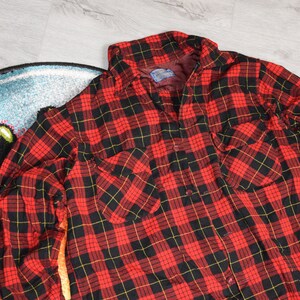 Könnte beinhalten: Rotes und schwarzes kariertes Flanellhemd mit langen Ärmeln und Knopfleiste. Das Hemd hat zwei Brusttaschen.